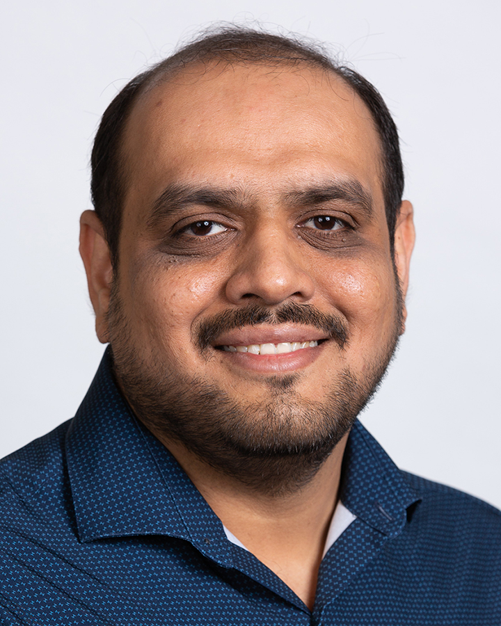 Tushar Patel wearing a blue button down shirt in front of a white backdrop