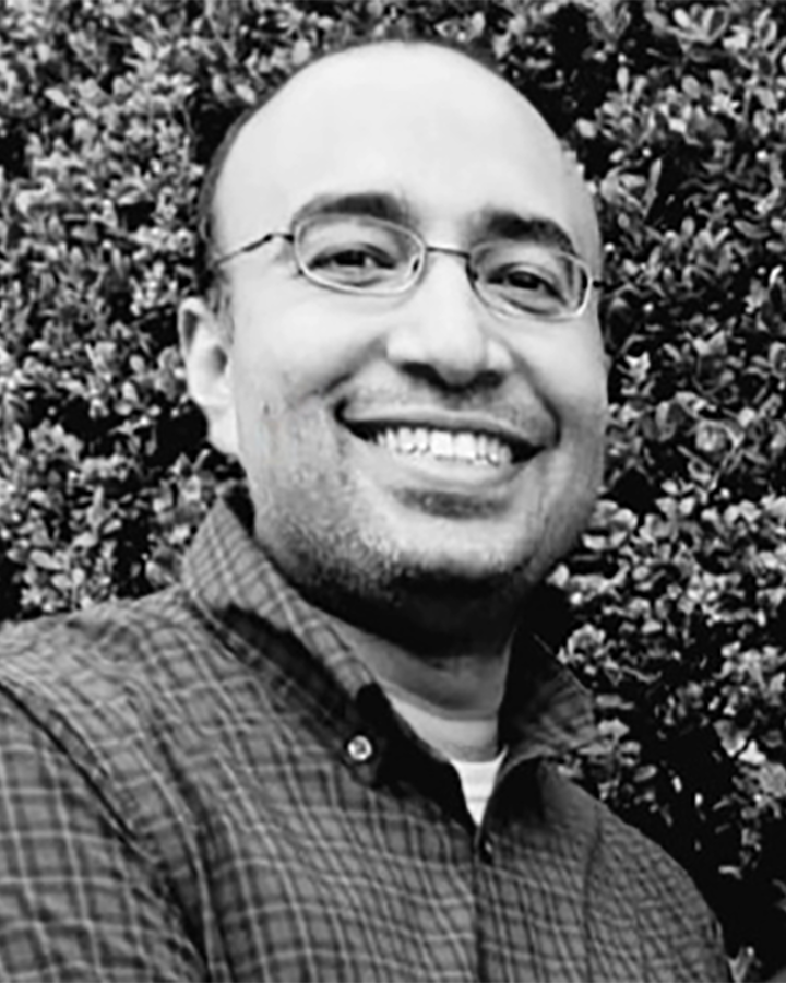 Black and white photo of Robbins Puthenveetil in front of a tall hedge