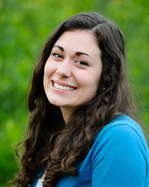 Lauren Walling, smiling, with long brown curly hair and a blue sweater