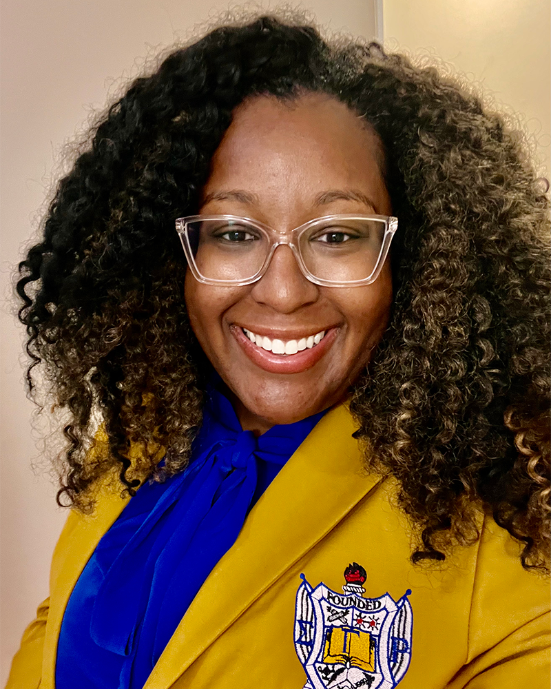 Aisha Burton in a gold blazer with the Sigma Gamma Rho crest