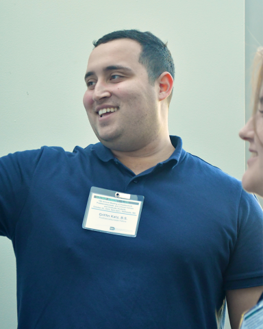 A fellow in a dark blue polo shirt smiles. Another fellow smiles from the edge of the photo.