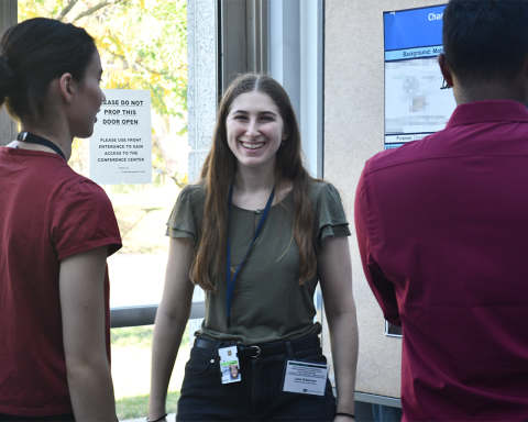 A fellow with long center-parted hair smiles broadly at the camera as two other fellows look on