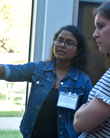 A fellow wearing glasses and a denim jacket points to something out of frame to the left. To their left, a fellow in a striped shirt looks on