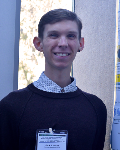 A fellow in a button-down shirt and dark sweater smiles for the camera