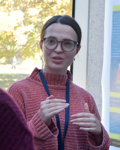 A fellow in a slouchy red sweater, rounded glasses, hair pulled back into a ponytail