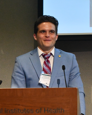 A fellow in a blue-gray suit smiles from behind a lectern