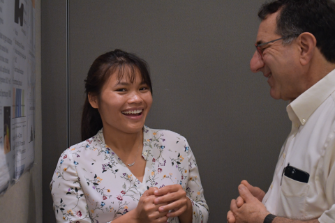 A trainee smiles widely while chatting with a senior investigator, also smiling