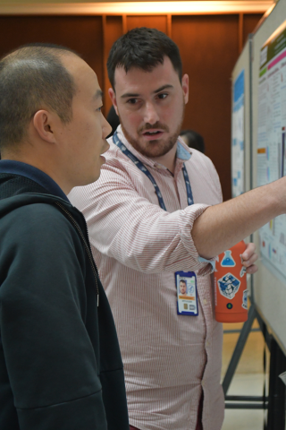 A fellow, holding a water bottle, speaks to another trainee at the poster session